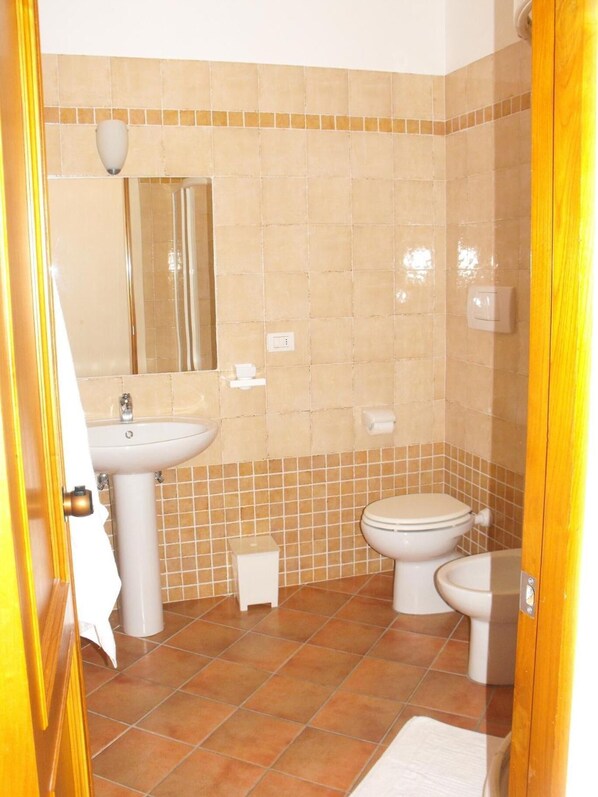 A bathroom with a sink, mirror, toilet, and a small trash bin. - Villa Etruria Guest House (Pitigliano)