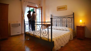 A bedroom with a metal bed frame, a bedside table with a lamp, and a window with curtains. - Villa Etruria Guest House (Pitigliano)