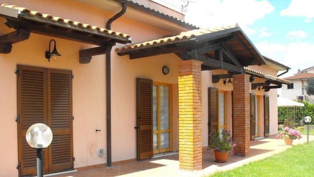 A two-story house with a tiled roof, wooden shutters, and a brick column. - Villa Etruria Guest House (Pitigliano)