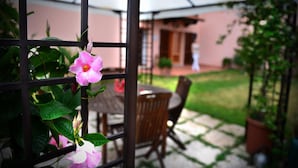A patio area with a table and chairs, a pergola with flowers, and a building in the background. - Villa Etruria Guest House (Pitigliano)