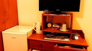 A compact room with a wooden dresser, a television, a small refrigerator, and a clock. - Villa Etruria Guest House (Pitigliano)