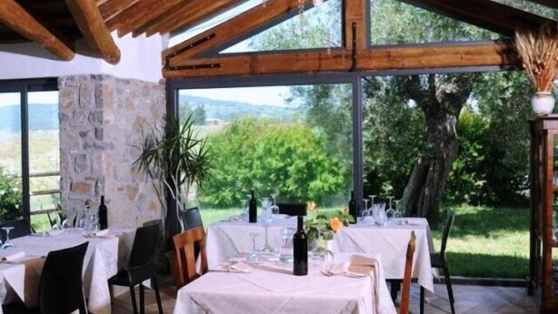An outdoor dining area with tables set for a meal, stone pillars, and a view of greenery. - Agriturismo Le Ginestre (Manciano)