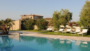 A swimming pool with lounge chairs, surrounded by greenery and a building in the background. - Agriturismo Le Ginestre (Manciano)