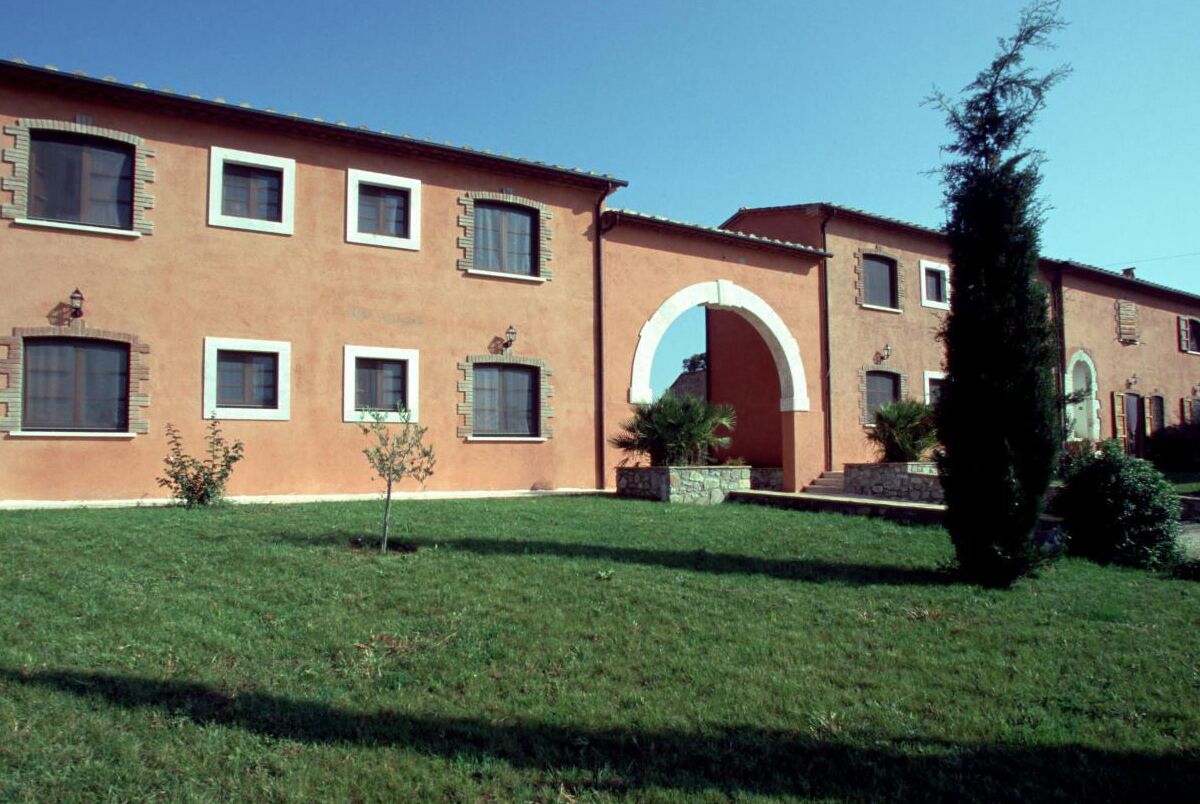 Un edificio de dos plantas con fachada roja, múltiples ventanas y una entrada central en arco.