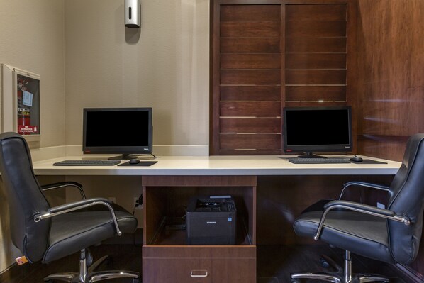 A workspace with two monitors, a printer, and two office chairs.