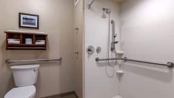 Un baño con inodoro blanco, ducha con barras de apoyo y toallero con toallas.