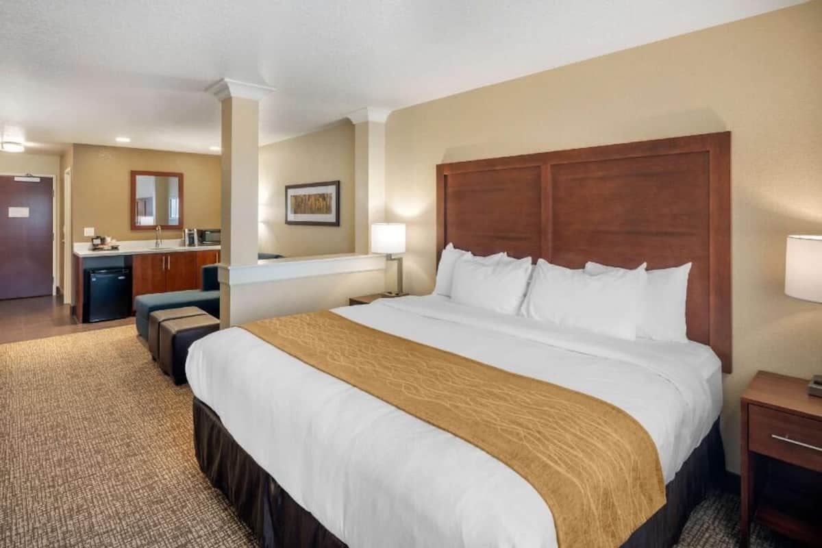 Ein Hotelzimmer mit einem großen Bett, einem Schreibtisch mit Stuhl, einer kleinen Küchenzeile und einem Badezimmer.
