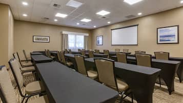 A conference room with multiple tables and chairs, a projector screen, and framed pictures on the walls.
