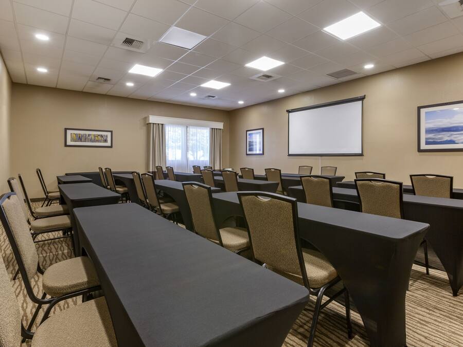 A conference room with multiple tables and chairs, a projector screen, and framed pictures on the walls.