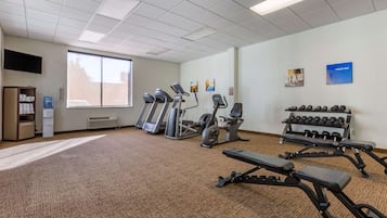 A gym with treadmills, elliptical machines, a bench press, and a rack of dumbbells.