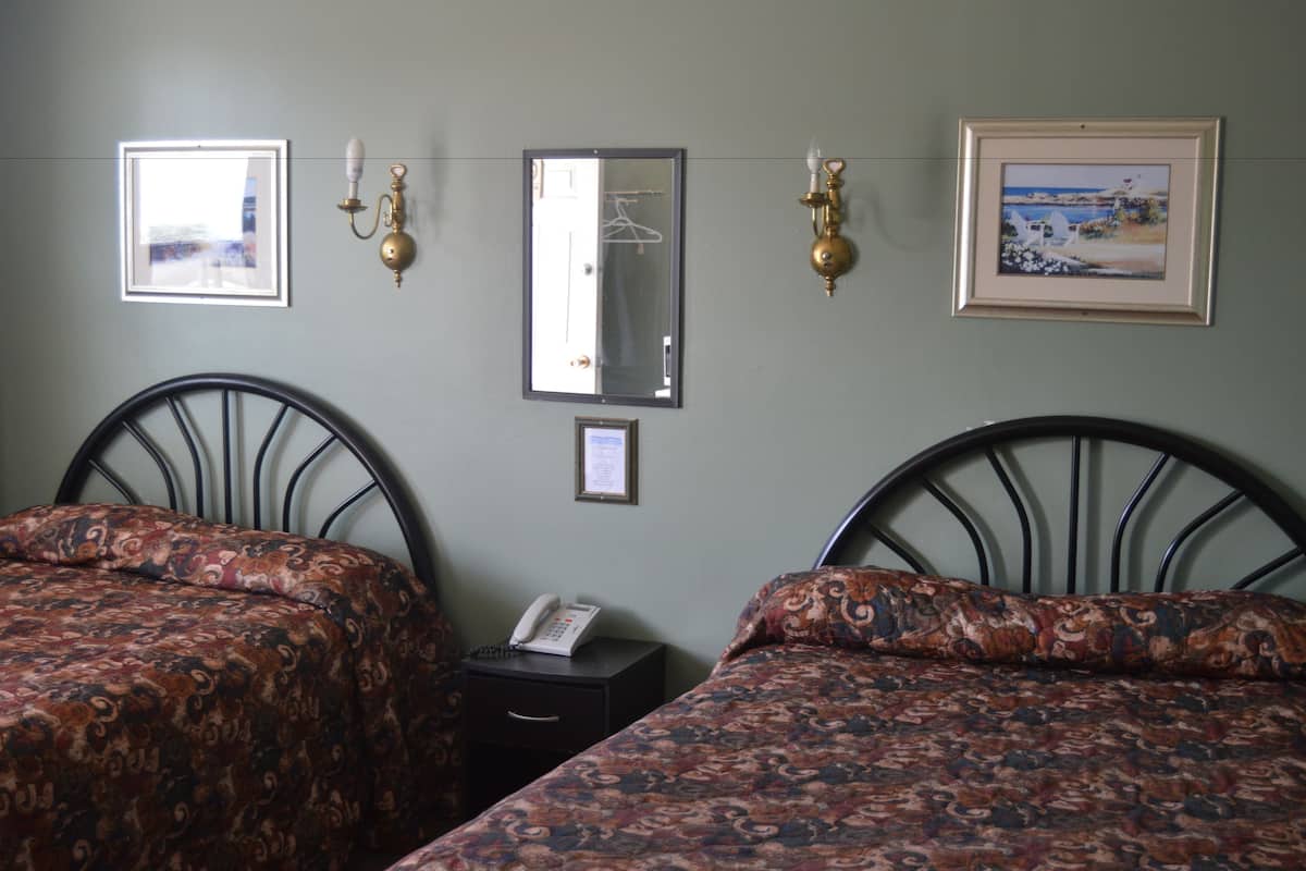 A hotel room with two beds, a small bedside table with a phone, and a wall-mounted mirror.