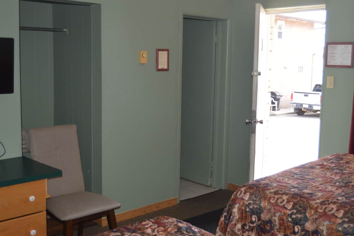 A room with a bed, a chair, a desk, and a door leading to a parking area.