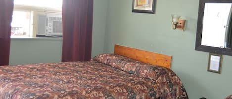 A bedroom with a patterned bedspread, a wooden headboard, a bedside telephone, and a framed picture on the wall.