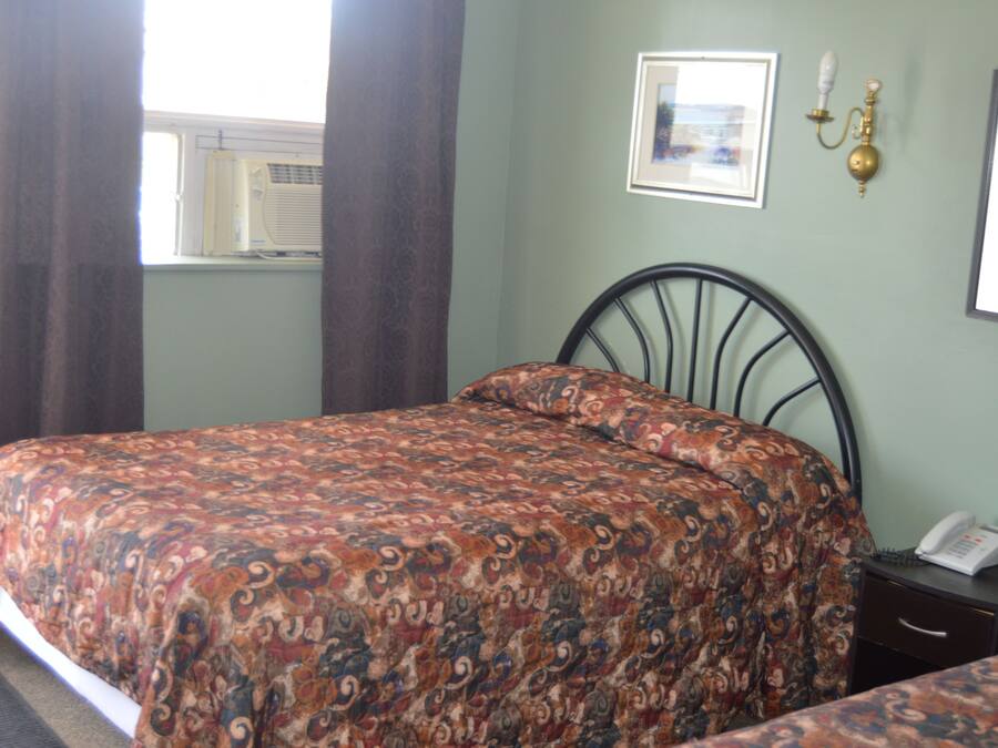 A bedroom with a bed, a bedside table, a lamp, and a window with curtains.