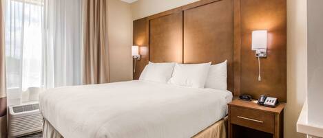 A hotel room with a large bed, two bedside lamps, a nightstand with a phone, and a window with curtains.