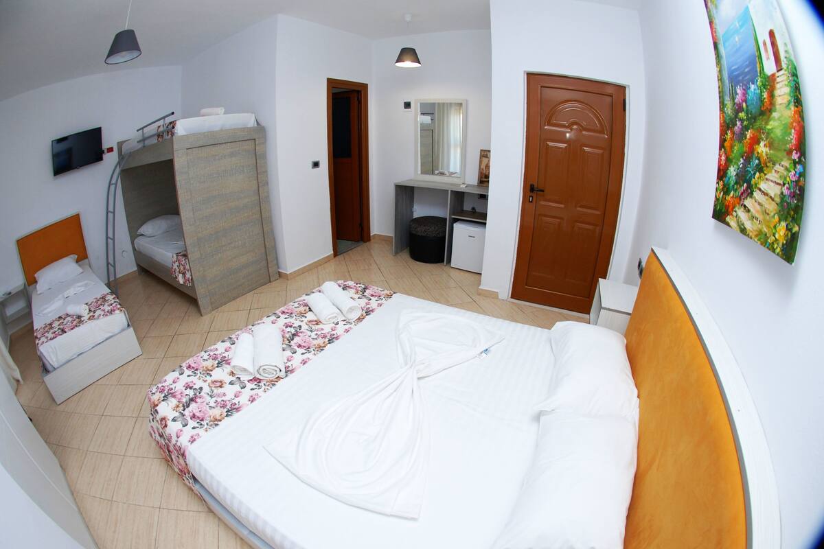 A hotel room with a bunk bed, a desk with a mirror, a small trash bin, and a door.