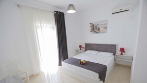 A clean, modern hotel room with a large bed, white walls, and a painting of a cityscape. - Hotel Horizont (Aliko)
