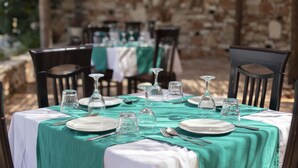 An outdoor dining area with tables set for a meal, featuring clear glassware and plates, and a stone wall in the background. - Hotel Horizont (Aliko)