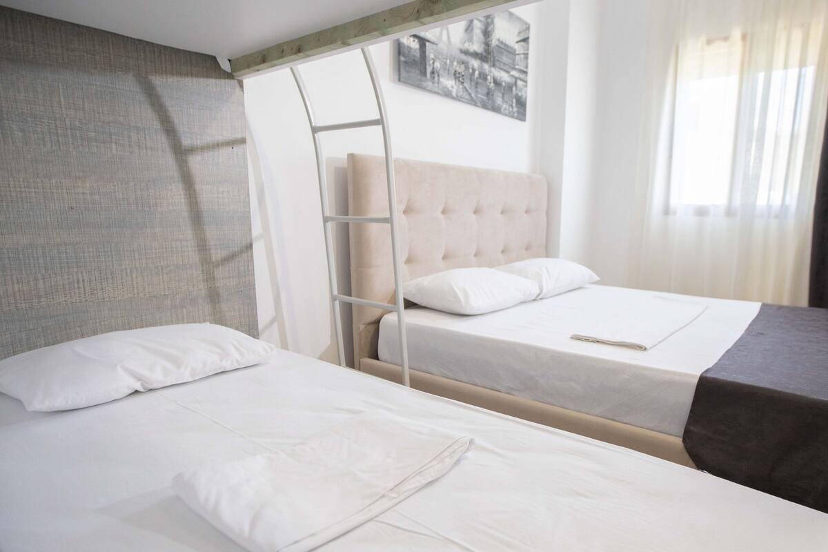 Two single beds with white linens, a wooden ladder, and a beige headboard.