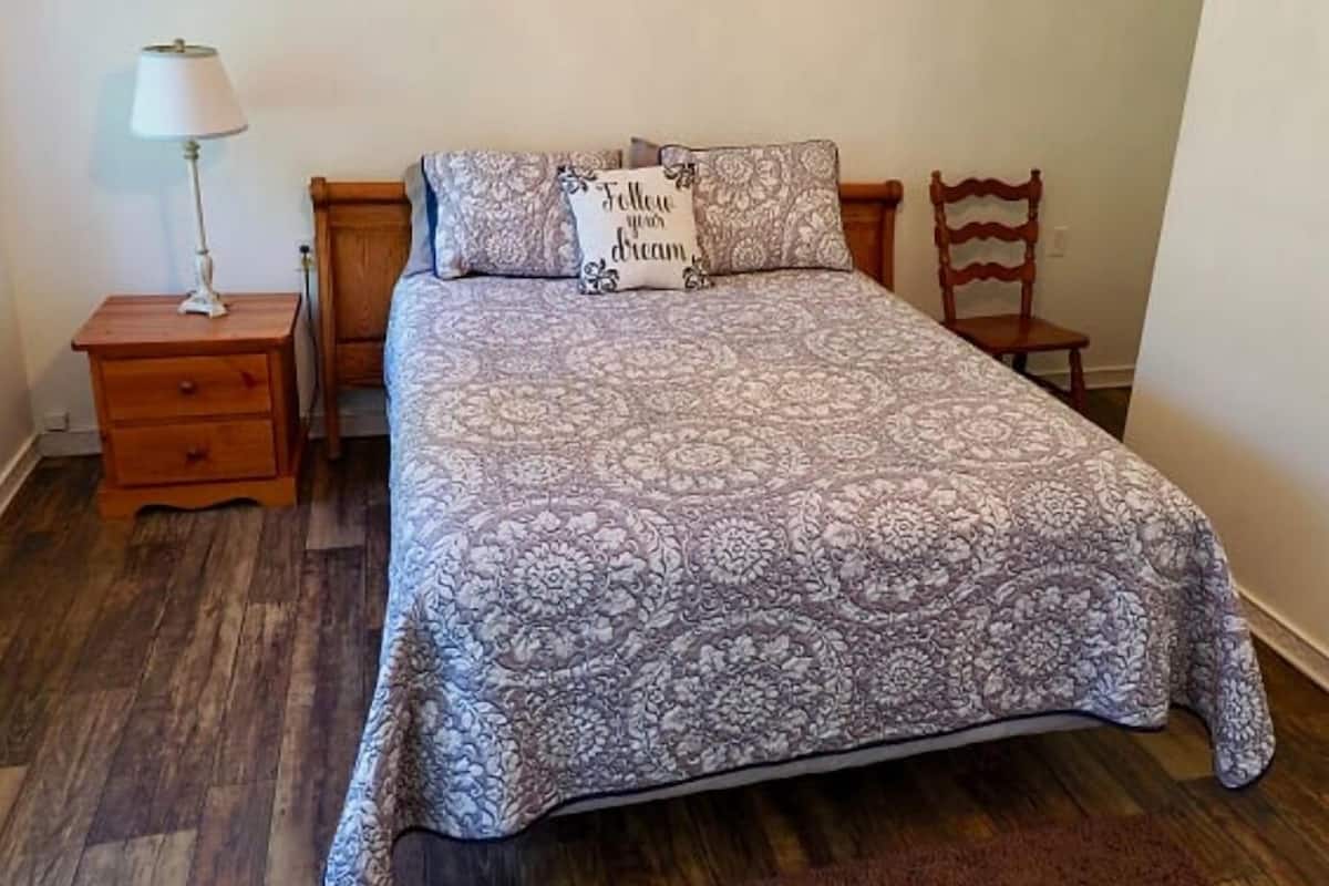 A bed with a floral-patterned bedspread, a bedside lamp, and a wooden nightstand.