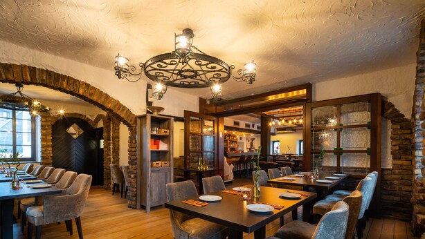 A restaurant with a rustic interior, featuring wooden tables and chairs, a brick archway, and a chandelier. - Landhotel Fettehenne (Leverkusen)