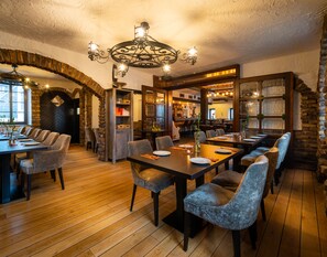 A restaurant with a rustic interior, featuring wooden tables and chairs, a brick archway, and a chandelier. - Landhotel Fettehenne (Leverkusen)