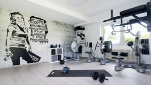 A gym with a motivational mural, weightlifting equipment, and a window providing natural light. - Landhotel Fettehenne (Leverkusen)