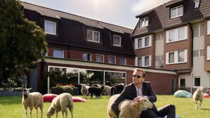 A person sitting on a bean bag chair in a grassy area with sheep in the background. - Landhotel Fettehenne (Leverkusen)