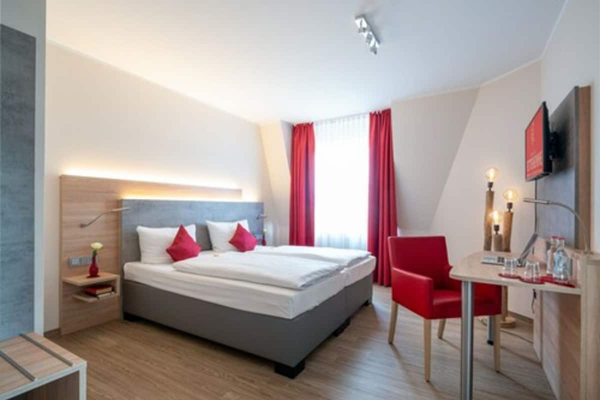 A modern hotel room with a large bed, a desk with a chair, and a TV mounted on the wall.