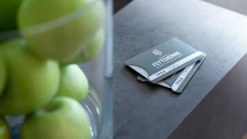 A glass container with green apples and a small booklet labeled 'FETTEHEMNE 1966' on a dark surface.