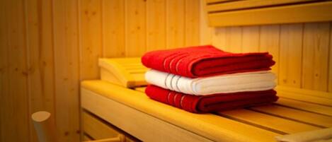 A wooden cabin with a bed, a chair, and a stack of folded towels.