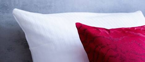 A pillow with a white and red patterned cover against a textured grey wall.