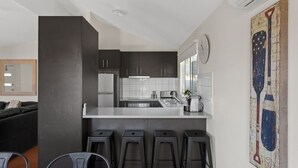 A modern kitchen with dark cabinets, a white countertop, and a bar area with stools. - Cowes Retreat - *Pet Friendly* Holiday House!!! (Cowes)