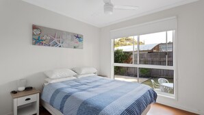 A bedroom with a bed, nightstand, and a window with a view of the backyard. - Cowes Retreat - *Pet Friendly* Holiday House!!! (Cowes)