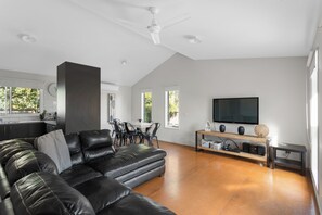 Ein modernes Wohnzimmer mit einem schwarzen Ledersofa, einem Essbereich mit weißem Tisch und einem an der Wand befestigten Flachbildfernseher.