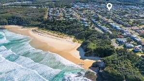 An aerial view of a coastal town with a beach, residential area, and a notable mountain in the background.