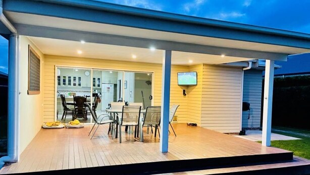 A modern house with a covered patio, a dining area with chairs and a table, and a TV mounted on the wall.