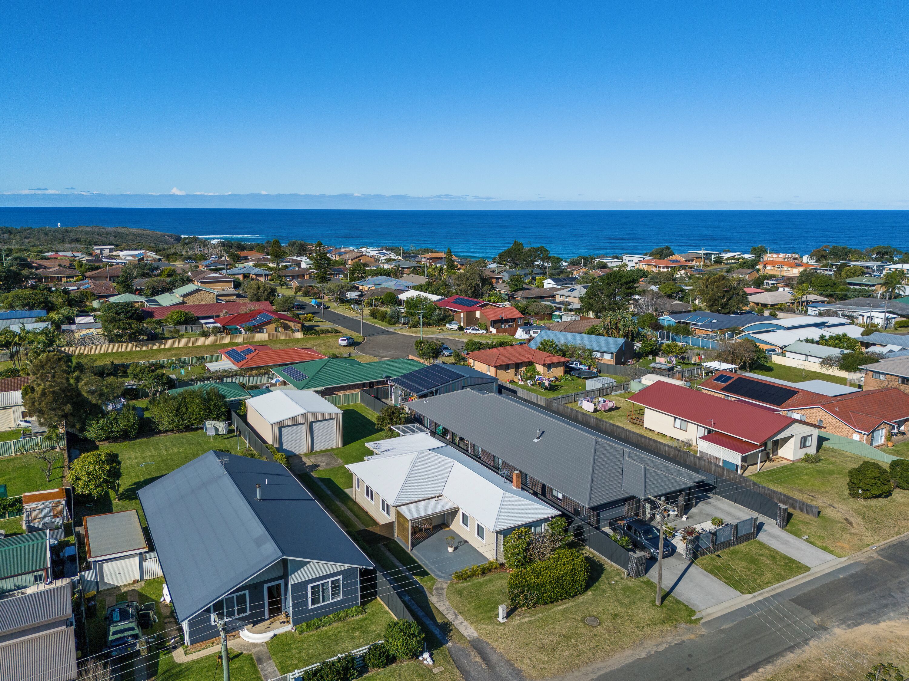 An aerial view of a coastal residential area with houses, a marina, and a clear view of the ocean.