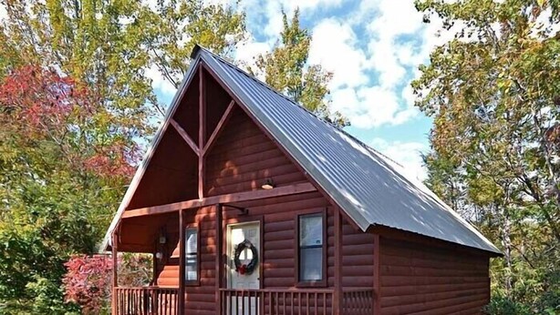A small, single-story log cabin with a porch and a decorative wreath on the door. - Gatlinburg Cabin Free Tickets, Heart Whirlpool, Hot Tub, King Bed, Fast Internet (Gatlinburg)