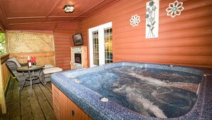 A hot tub with a wooden deck, a wicker sofa, and a small table with a bottle and glasses. - Gatlinburg Cabin Free Tickets, Heart Whirlpool, Hot Tub, King Bed, Fast Internet (Gatlinburg)