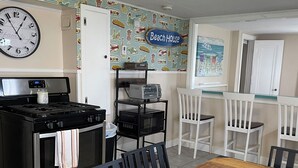 A kitchen with a clock, a toaster, and a microwave. There is a dining table with chairs and a tray of snacks. - Lower deck, Salisbury Beach, Melo's Beach House Rentals  (Salisbury)