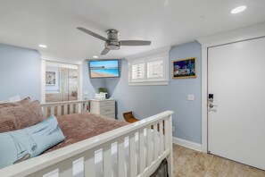 Un dormitorio con cama, ventilador de techo, televisor, ventana con persianas y puerta.