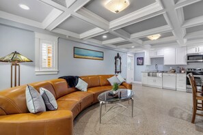 A modern living room with a leather sofa, a glass coffee table, and a kitchen in the background. - Croton House II " First Floor Unit " (New Smyrna Beach)