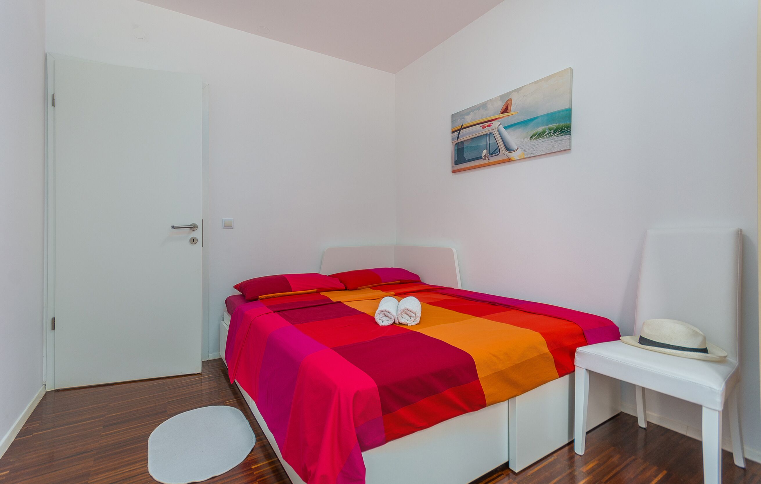 Un dormitorio con una cama, un banco blanco, un cuadro y una puerta.