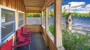 A covered porch with a view of a river, red chairs, and a fishing rod.
