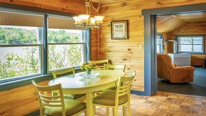 A dining area with a wooden table and chairs, a chandelier, and a view of greenery outside.