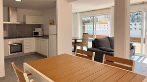 Eine moderne Küche mit weißen Schränken, einer Mikrowelle und einem Kühlschrank. Es gibt einen Essbereich mit einem Holztisch und Stühlen.