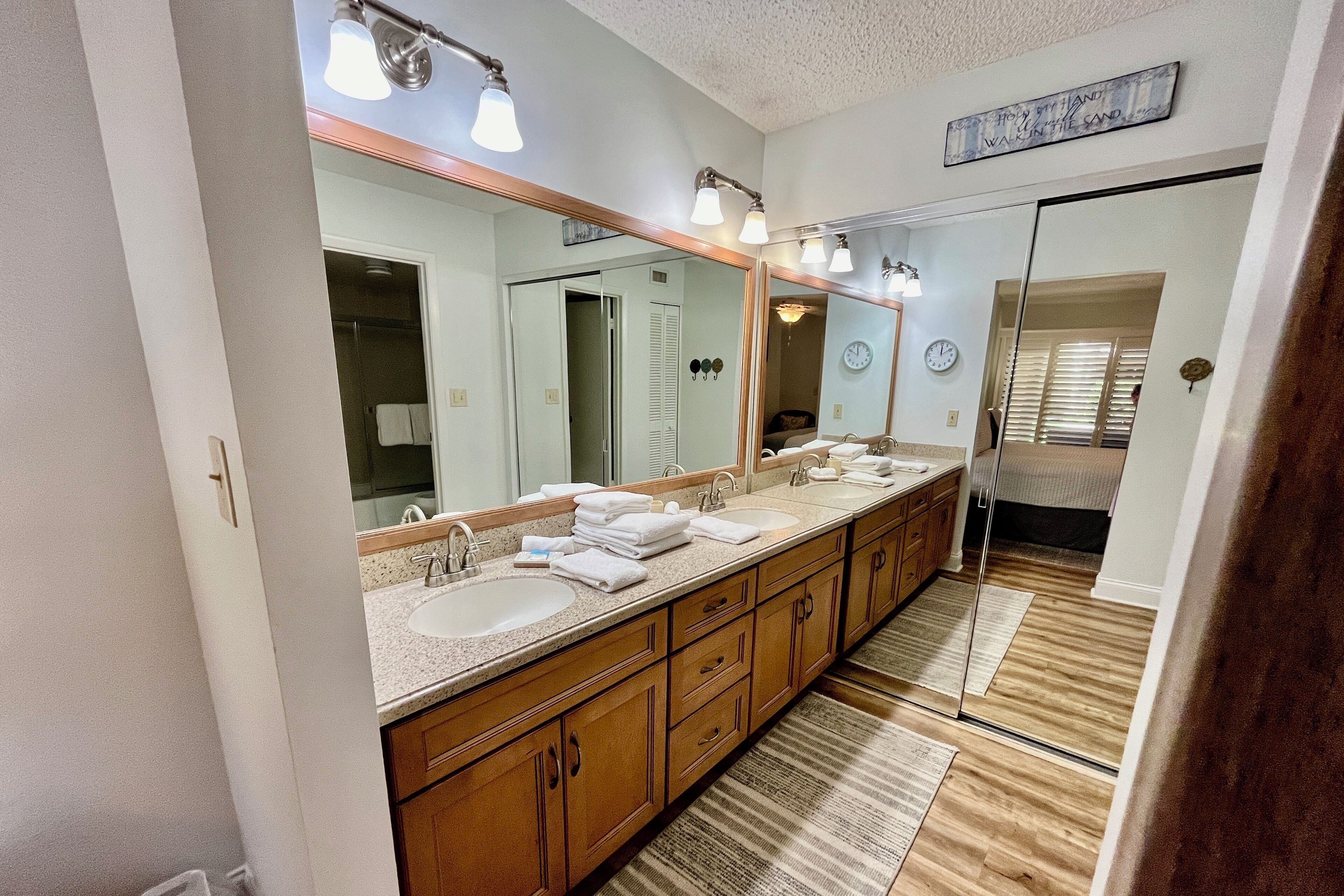 A bathroom with a large mirror, two sinks, wooden cabinets, and a striped rug.