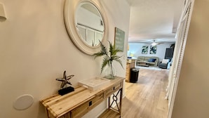 A wooden console table with a mirror, decorative items, and a potted plant in a hallway leading to a living area. - FREE FUN during your stay in this Gold-rated condo with beautiful ocean view and easy access to the pool and beach! (Saint Augustine)