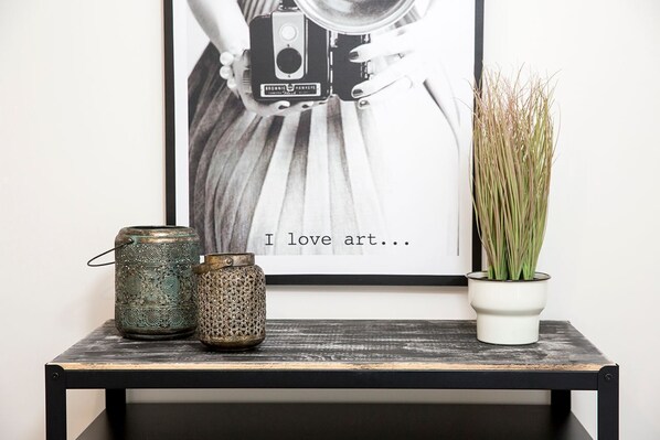 A framed artwork on a wall, two decorative metal containers, and a potted plant on a wooden shelf.